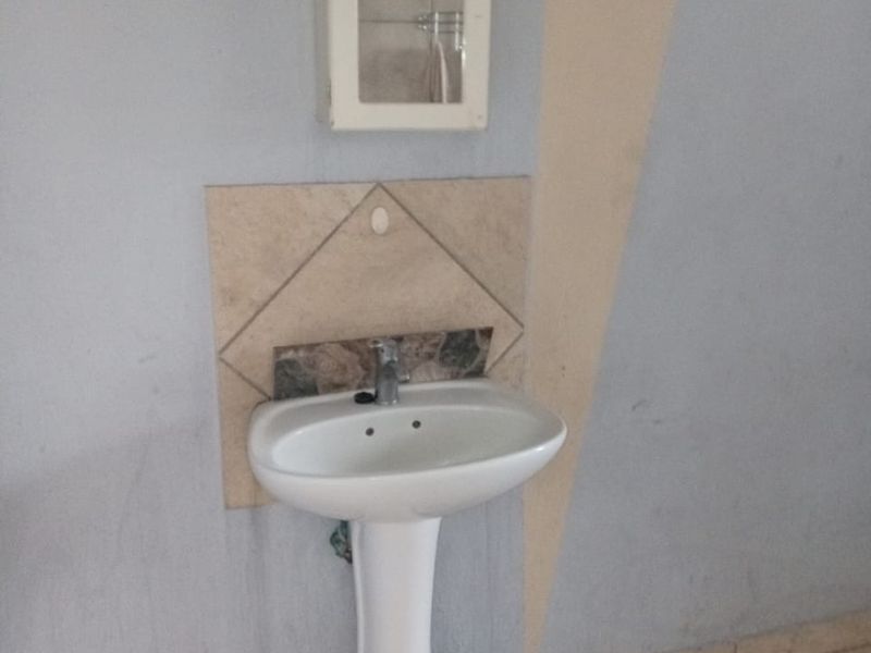 A basic bathroom area featuring a pedestal basin, tiled splashback, and a wall-mounted medicine cabinet with ceramic floor tiling.