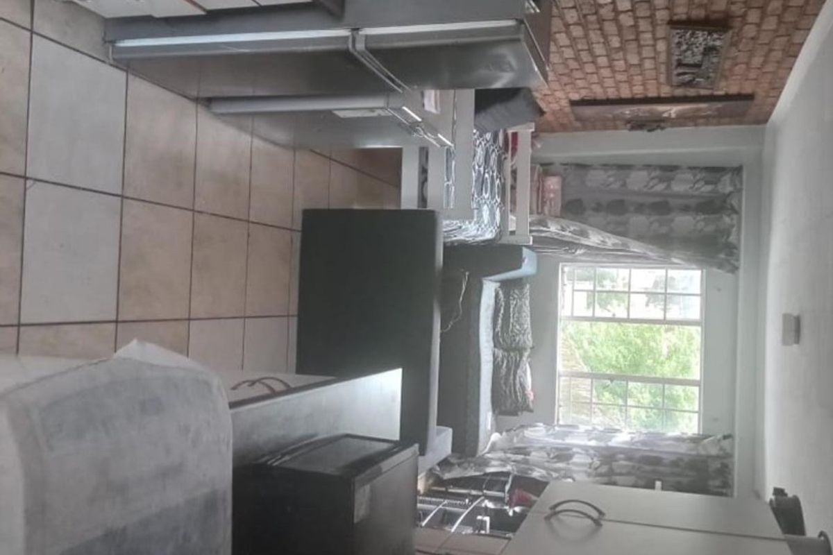 A kitchen area featuring tiled flooring, built-in cabinetry, and an exposed brick wall, providing a functional layout with natural light from the window.