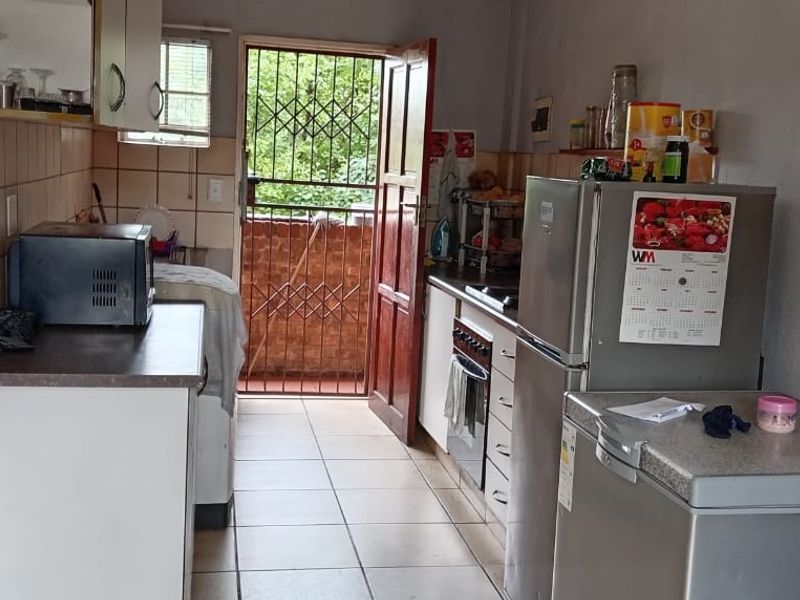 A functional kitchen featuring tiled flooring, a built-in oven, and an exposed brick feature wall, with direct access to an outdoor area via a security gate.