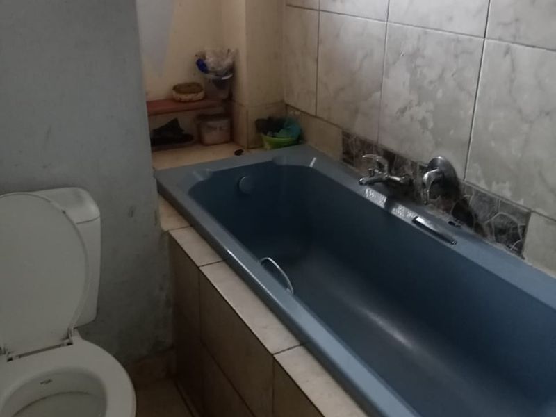 A functional bathroom featuring a built-in bathtub and toilet, requiring cosmetic updates to the wall finishes and tiling to improve its overall condition.