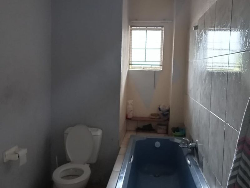 A functional bathroom featuring a built-in bathtub, toilet, and tiled wall finishes, currently requiring cosmetic updates and maintenance.