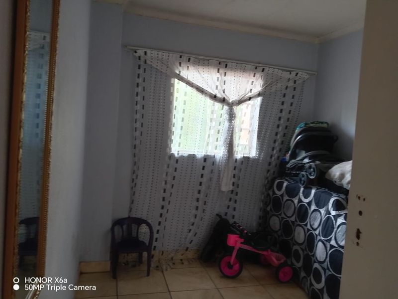 A bedroom featuring tiled flooring and a window with curtains, providing a functional space ready for personalization.