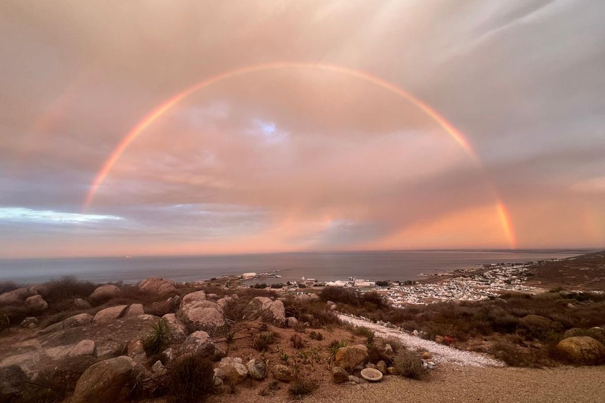 A scenic elevated view overlooking the coastline and town, featuring a prominent rainbow over the ocean horizon.