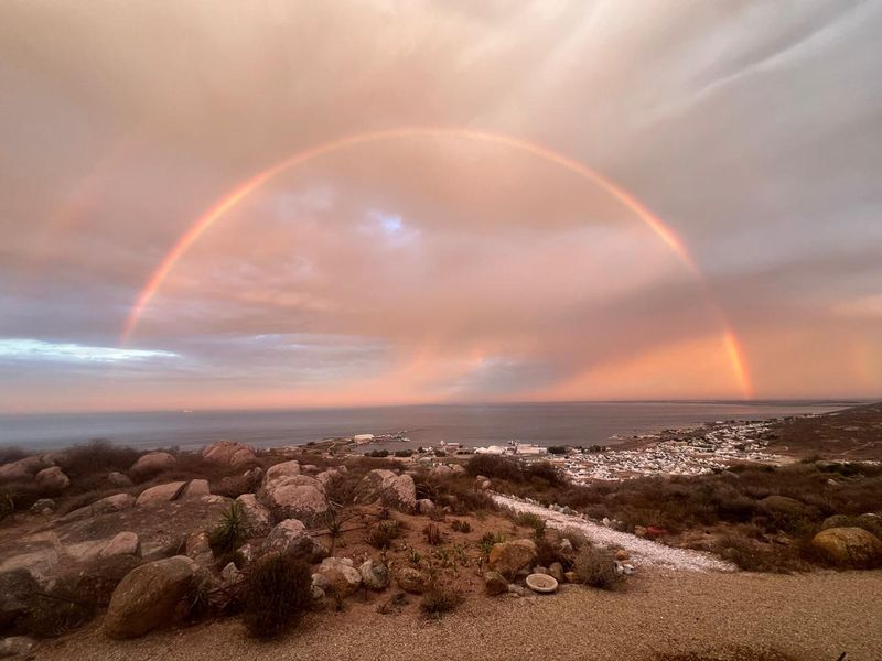A scenic elevated view overlooking the coastline and town, featuring a prominent rainbow over the ocean horizon.