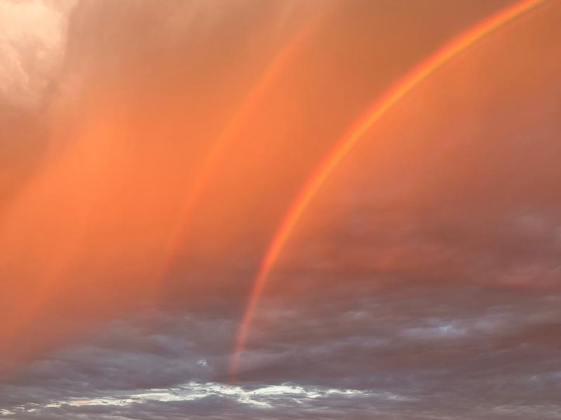 A scenic view of the ocean horizon featuring a double rainbow against a dramatic sunset sky.