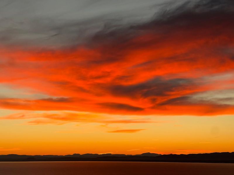 A scenic view of a vibrant sunset over a distant mountain range and water horizon.
