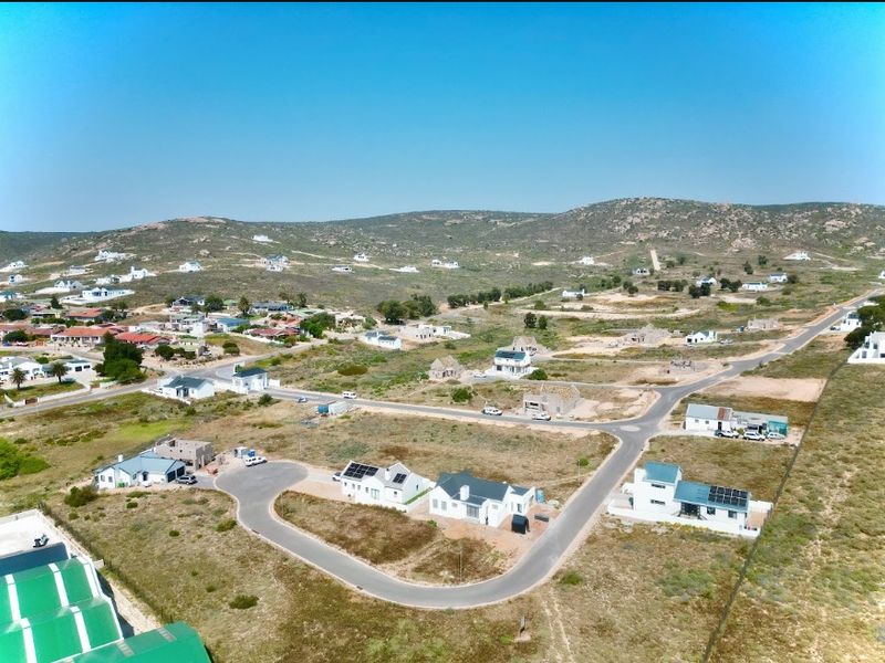 An aerial view of a coastal residential estate featuring multiple homes, paved roads, and surrounding natural landscape.