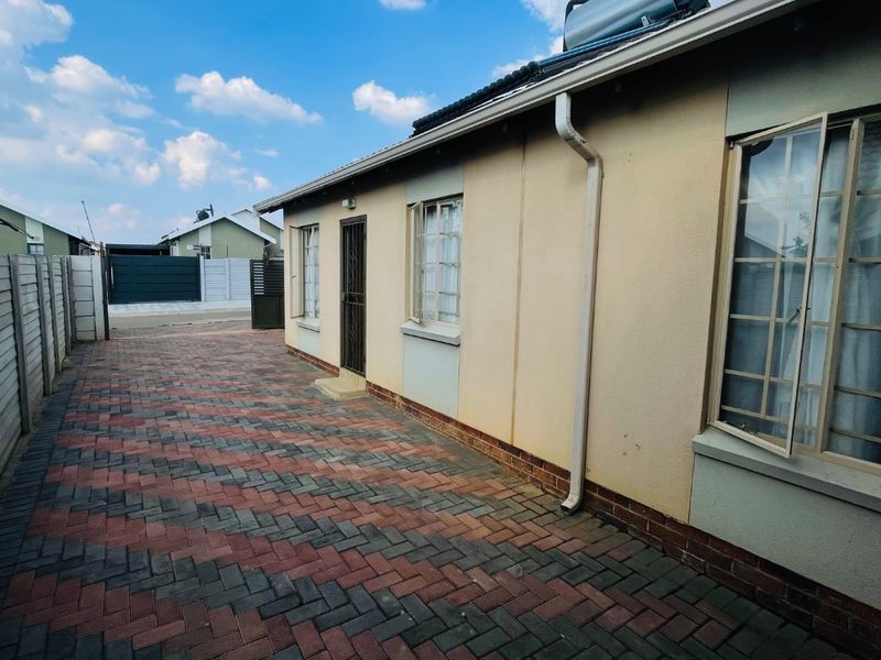 Rear exterior view of the property featuring a paved courtyard, security gate, and roof-mounted solar water heating system.
