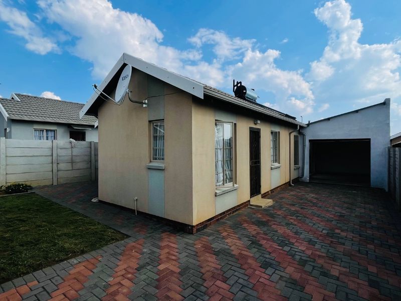Rear view of the property featuring a paved courtyard, attached garage, solar water heating system, and perimeter precast concrete walling.