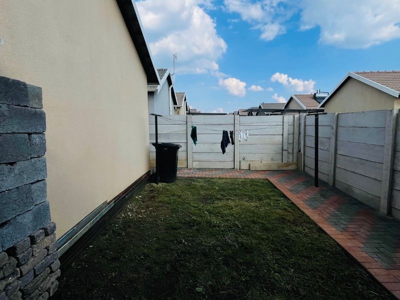 A rear garden area featuring a small lawn, paved pathways, and perimeter precast concrete walling.