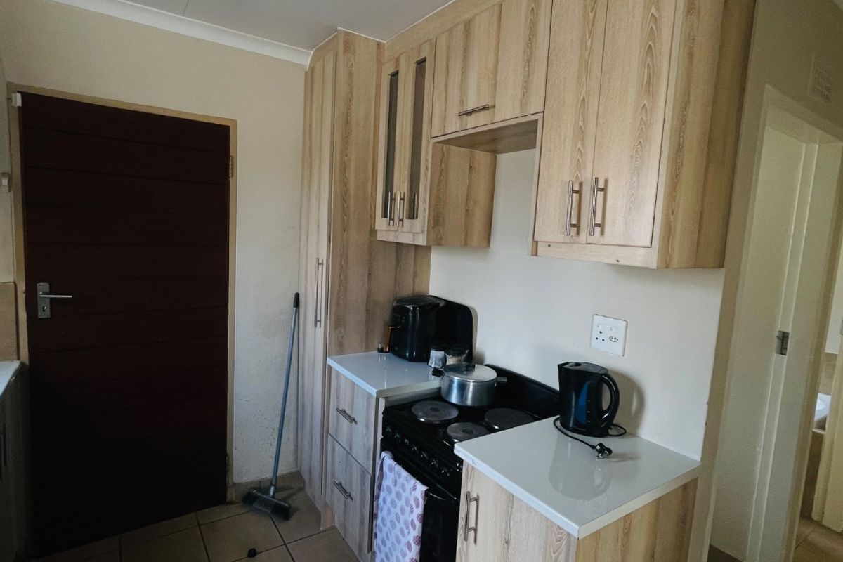 Compact kitchen featuring light wood-finish cabinetry, tiled flooring, and a freestanding stove, offering functional storage and preparation space.
