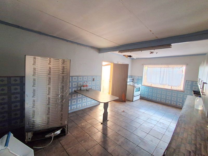A dated kitchen featuring tiled flooring, a built-in breakfast counter, and a freestanding stove, requiring significant cosmetic updates and ceiling repairs.