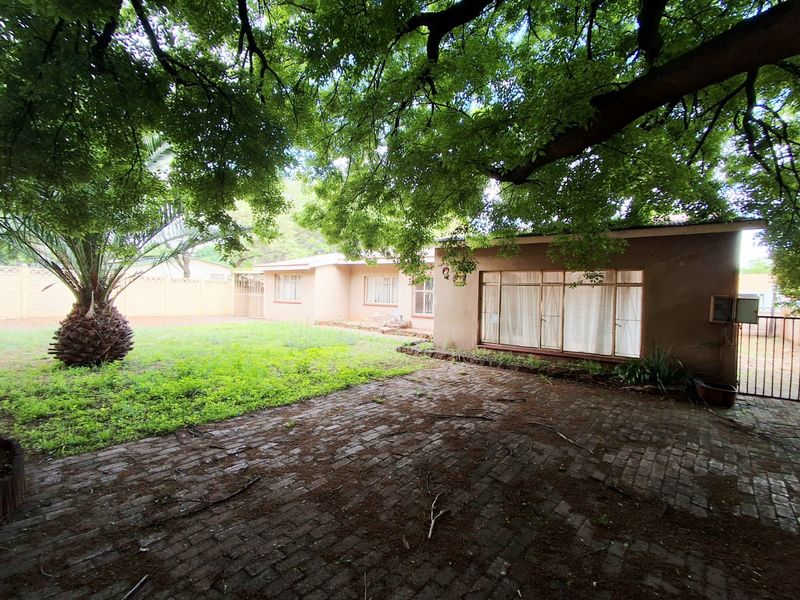Rear exterior view of the house featuring a brick paved patio, mature trees, and a garden area.