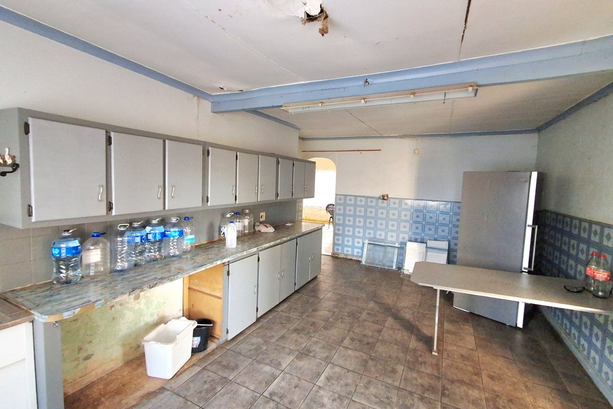 A spacious, dated kitchen featuring extensive cabinetry, tiled walls, and flooring, currently in need of significant renovation and ceiling repairs.