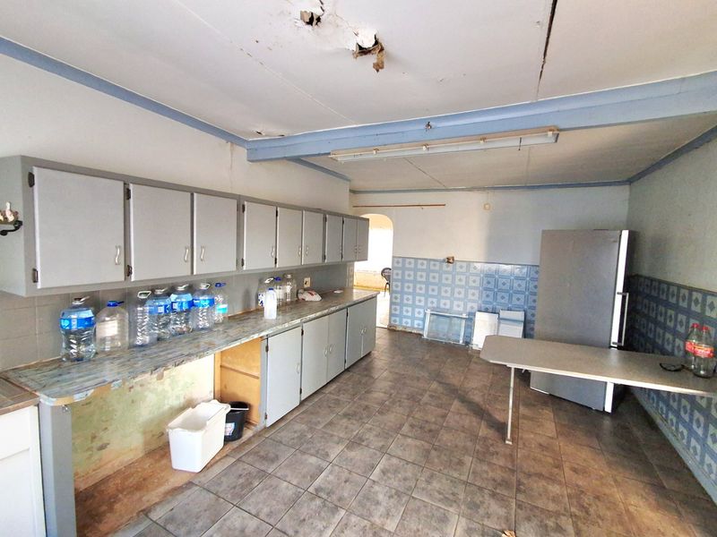 A spacious, dated kitchen featuring extensive cabinetry, tiled walls, and flooring, currently in need of significant renovation and ceiling repairs.