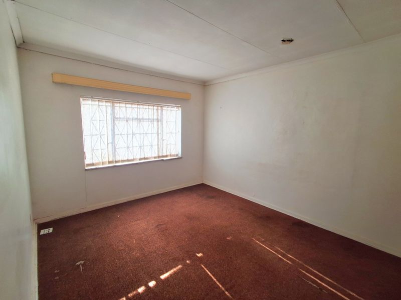 An empty bedroom featuring carpet flooring, security bars on the window, and a curtain pelmet, requiring cosmetic updates and repairs.