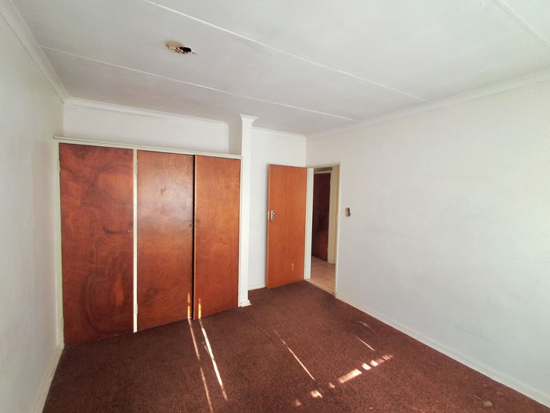 An empty bedroom featuring built-in wooden cupboards, carpeted flooring, and a doorway leading to an adjacent space.