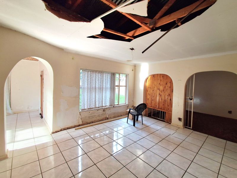 A vacant living room featuring ceramic floor tiles and arched architectural details, currently requiring significant ceiling and wall repairs.