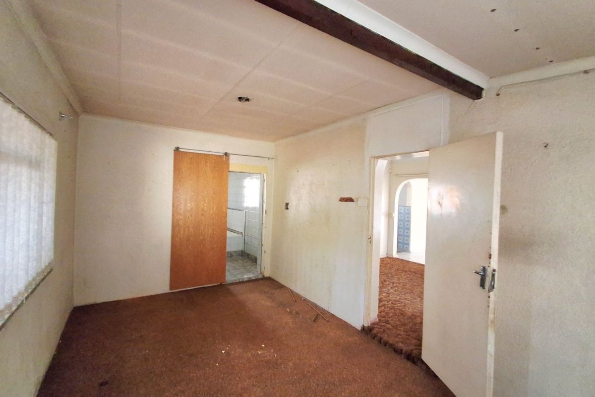 An empty bedroom featuring carpet flooring, an exposed ceiling beam, and a sliding door leading to an adjacent space.