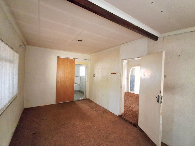 An empty bedroom featuring carpet flooring, an exposed ceiling beam, and a sliding door leading to an adjacent space.