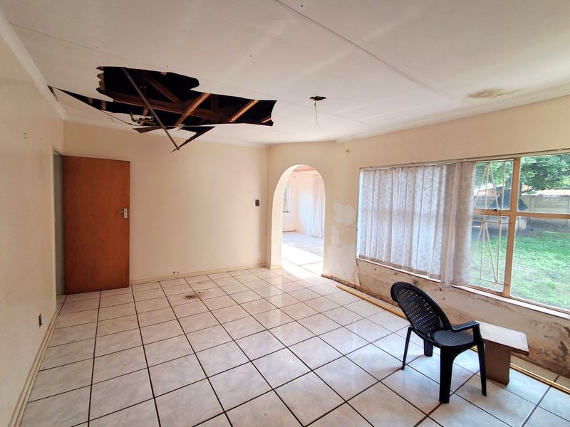 Spacious living area featuring ceramic floor tiles and an archway, currently requiring significant ceiling and wall repairs.
