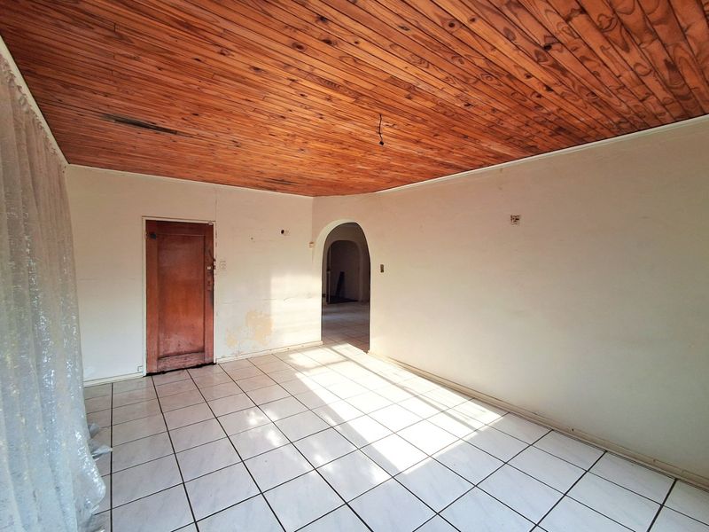 An empty living room featuring ceramic floor tiles, a wooden tongue and groove ceiling, and an arched doorway leading to an adjacent space.