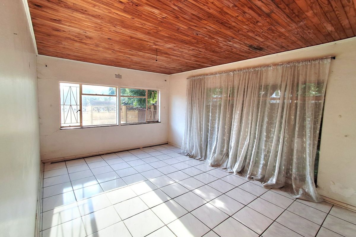 An empty living room featuring a timber tongue and groove ceiling, ceramic tiled flooring, and large windows with security bars.