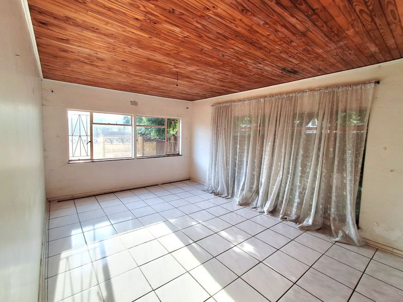 An empty living room featuring a timber tongue and groove ceiling, ceramic tiled flooring, and large windows with security bars.