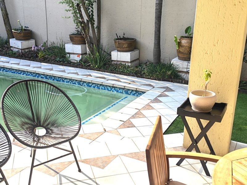 Outdoor patio area overlooking a swimming pool with tiled surround and perimeter boundary wall.