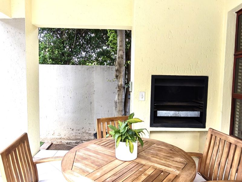 Covered patio area featuring a built-in braai, tiled flooring, and direct access to the garden through a timber-framed glass door.