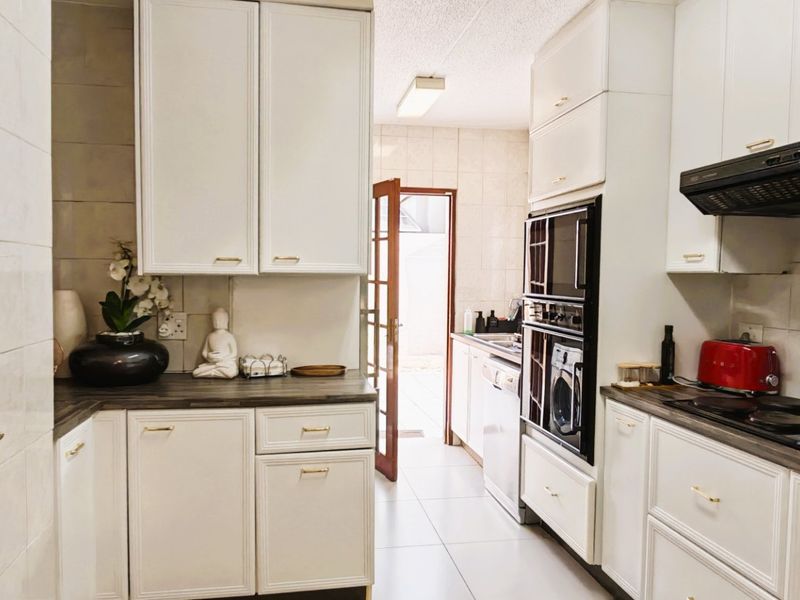 A functional kitchen featuring white cabinetry, dark laminate countertops, built-in oven, extractor fan, and tiled flooring with direct access to an outdoor area.