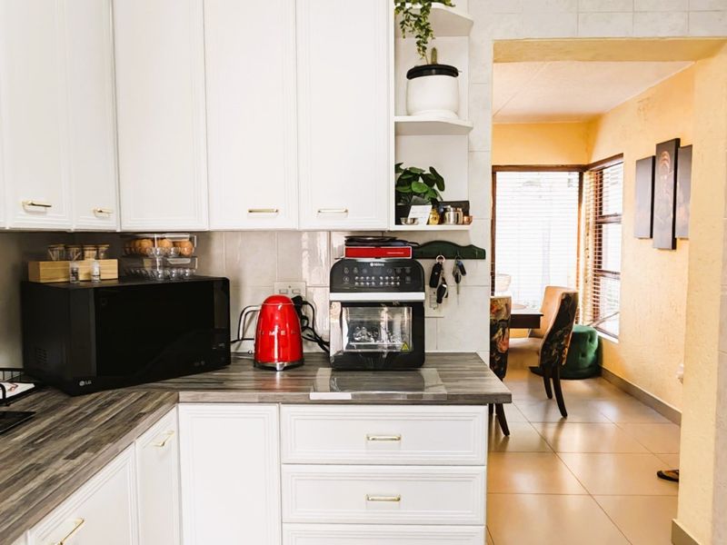 A functional kitchen featuring white cabinetry, laminate countertops, and a tiled backsplash, with an open transition to the adjacent dining area.