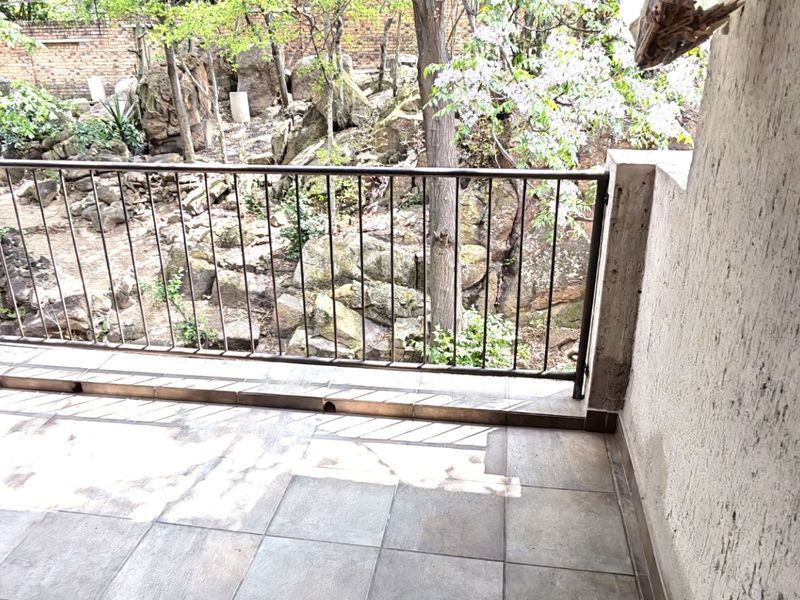 A covered balcony featuring tiled flooring and a metal balustrade, overlooking a natural rocky garden area.