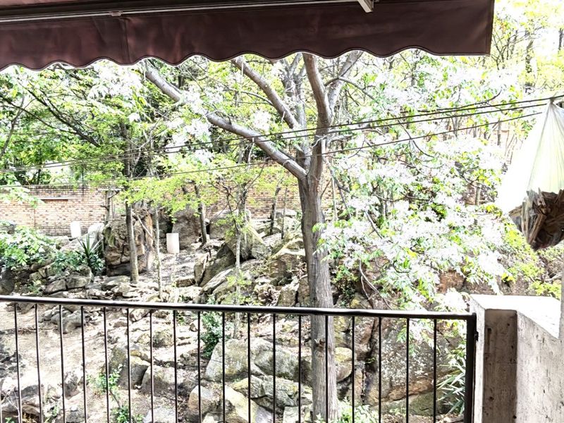A covered balcony area featuring a retractable awning and metal railing, overlooking a natural rocky garden setting.