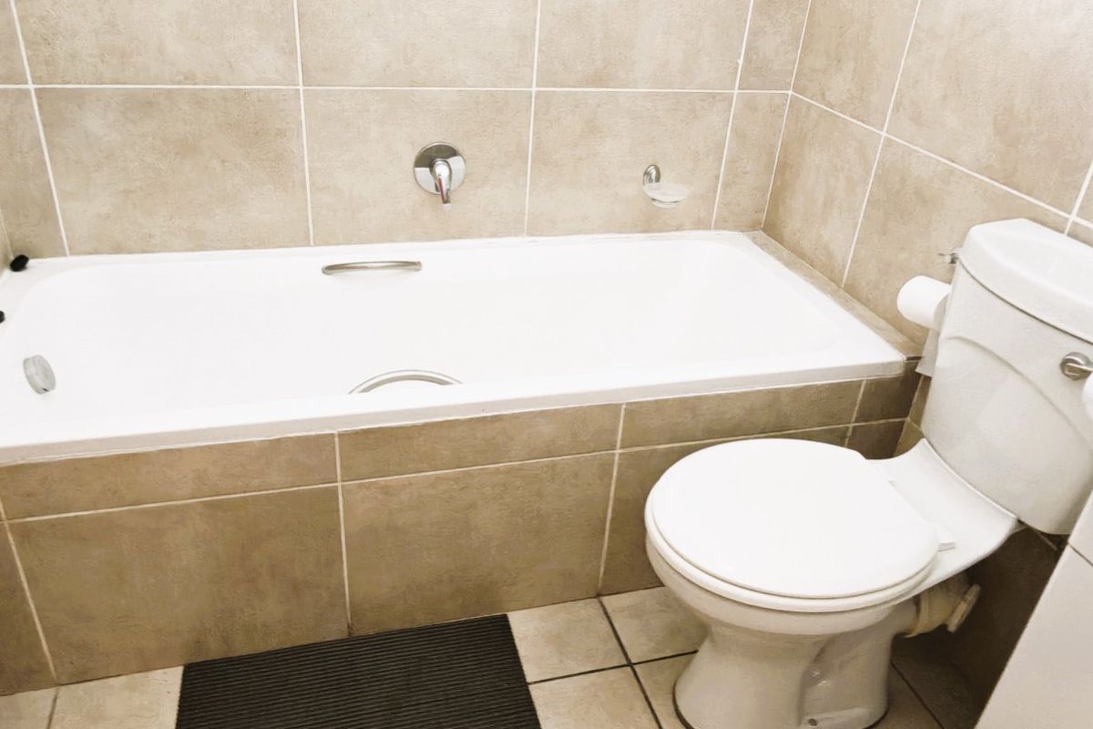 A clean, functional bathroom featuring neutral ceramic wall and floor tiles, a built-in bathtub, a standard toilet, and a pedestal sink.