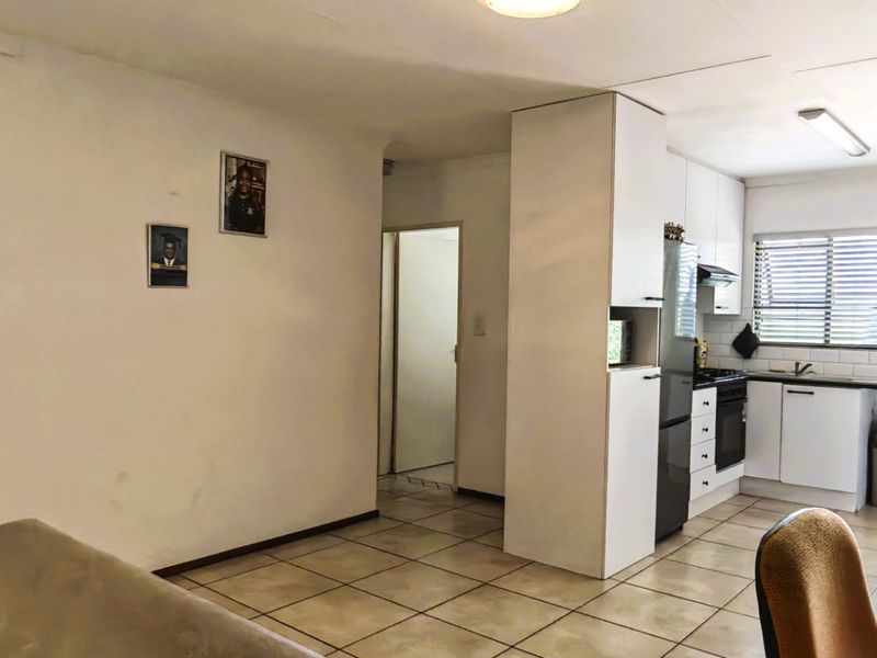 Open-plan living and kitchen area featuring tiled flooring, white cabinetry, and a functional kitchen layout with built-in appliances.