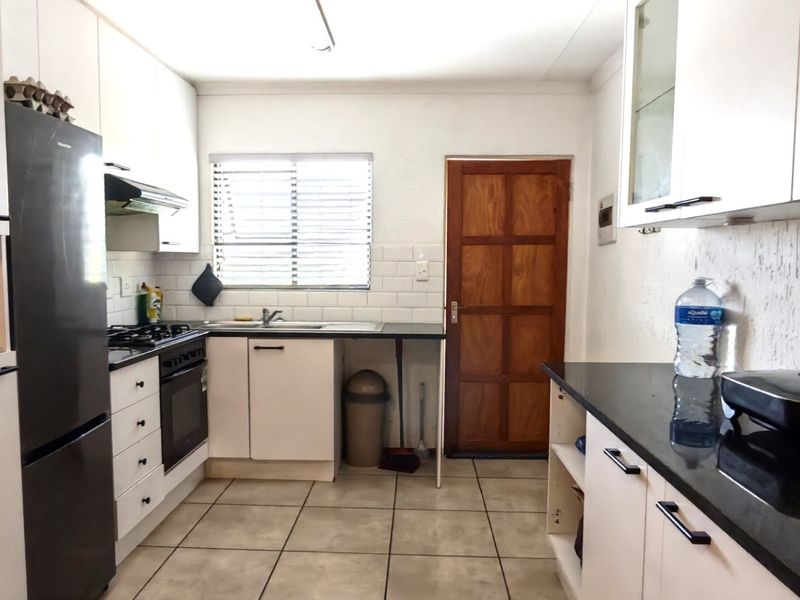 Functional kitchen featuring white cabinetry, granite countertops, subway tile backsplash, gas hob, and tiled flooring with direct access to an exterior door.