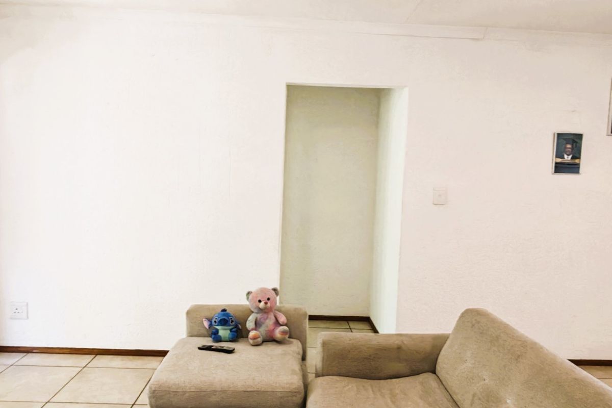 A simple living room area featuring neutral tiled flooring and plain white walls, providing a blank canvas for interior design.