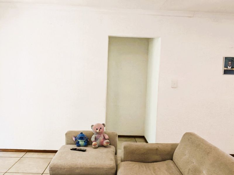 A simple living room area featuring neutral tiled flooring and plain white walls, providing a blank canvas for interior design.