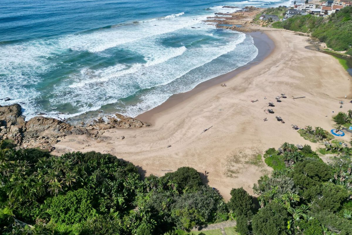An aerial view of the coastal beach and surrounding natural vegetation, highlighting the property's proximity to the ocean.