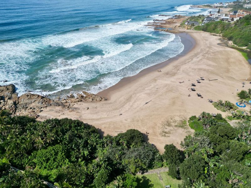 An aerial view of the coastal beach and surrounding natural vegetation, highlighting the property's proximity to the ocean.