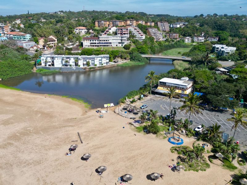 Aerial view of the coastal area featuring a river, bridge, beach, and adjacent parking facilities in a scenic residential setting.