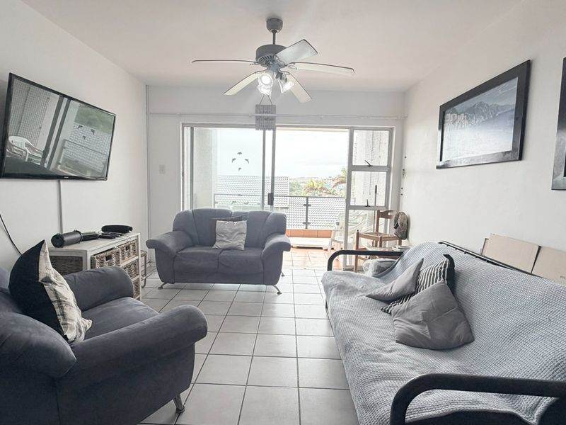 A living room featuring tiled flooring, a ceiling fan, and large sliding glass doors that provide access to an outdoor balcony area.