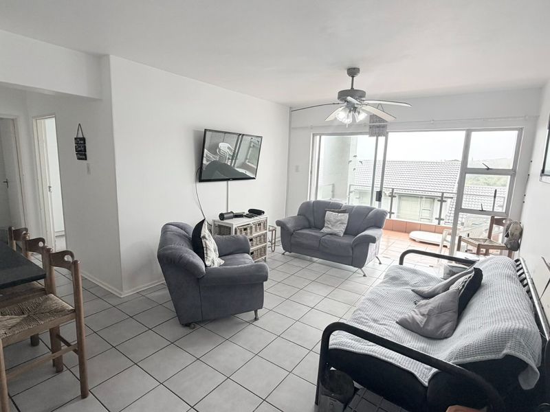 Open plan living area featuring tiled flooring, a ceiling fan, and direct access to an outdoor balcony through large sliding glass doors.