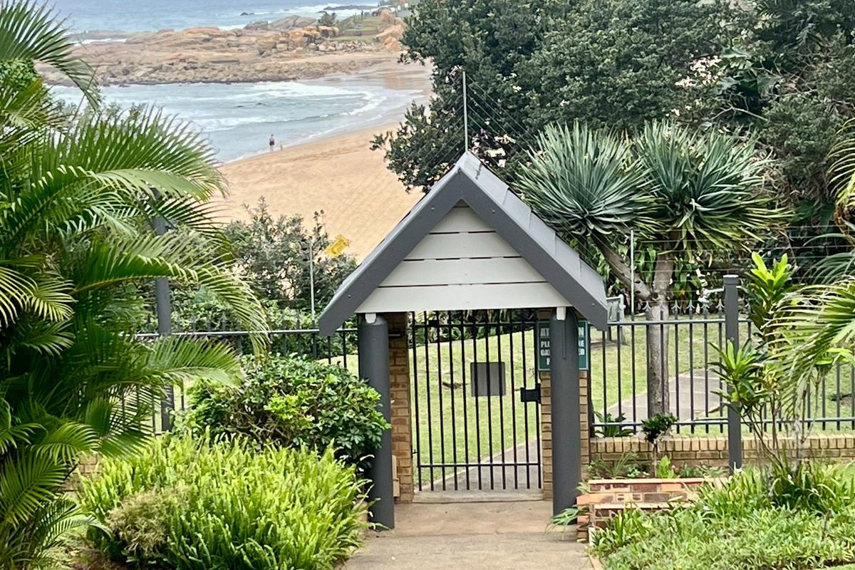 A secure gated entrance leading to a coastal garden area with views of the beach and ocean.