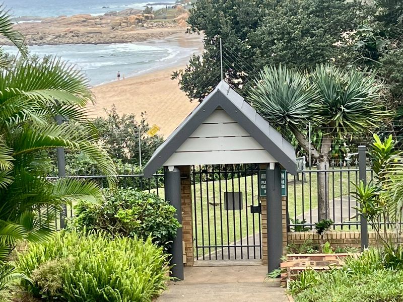 A secure gated entrance leading to a coastal garden area with views of the beach and ocean.