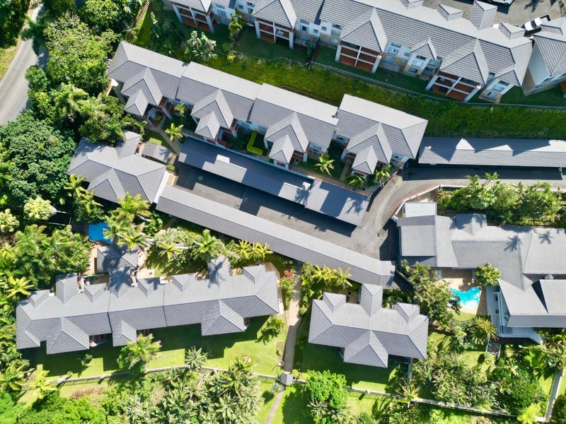 Aerial view of an apartment complex featuring multiple residential buildings with tiled roofs, swimming pools, landscaped gardens, and covered parking facilities.