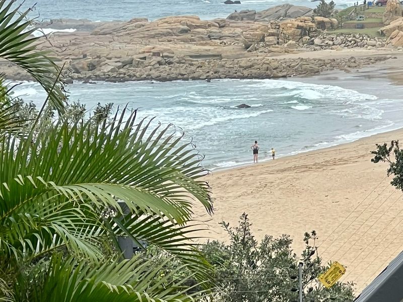 A scenic view overlooking a sandy beach and rocky coastline, showcasing the property's proximity to the ocean.