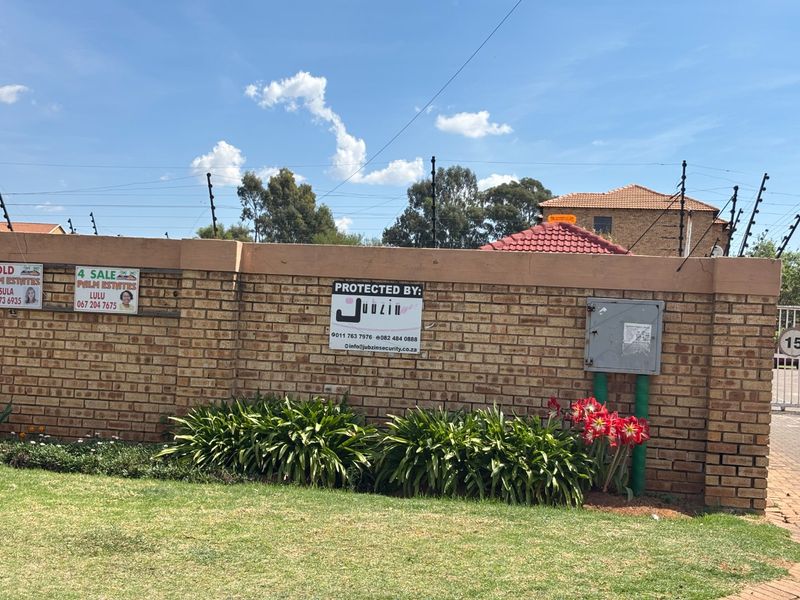 A view of the property's brick boundary wall featuring electric fencing, security signage, and a utility meter box.