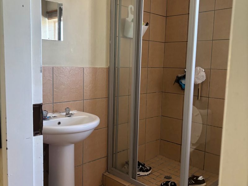 A compact bathroom featuring a pedestal basin and a shower enclosure with tiled walls and flooring, requiring cosmetic updates to modernize the space.